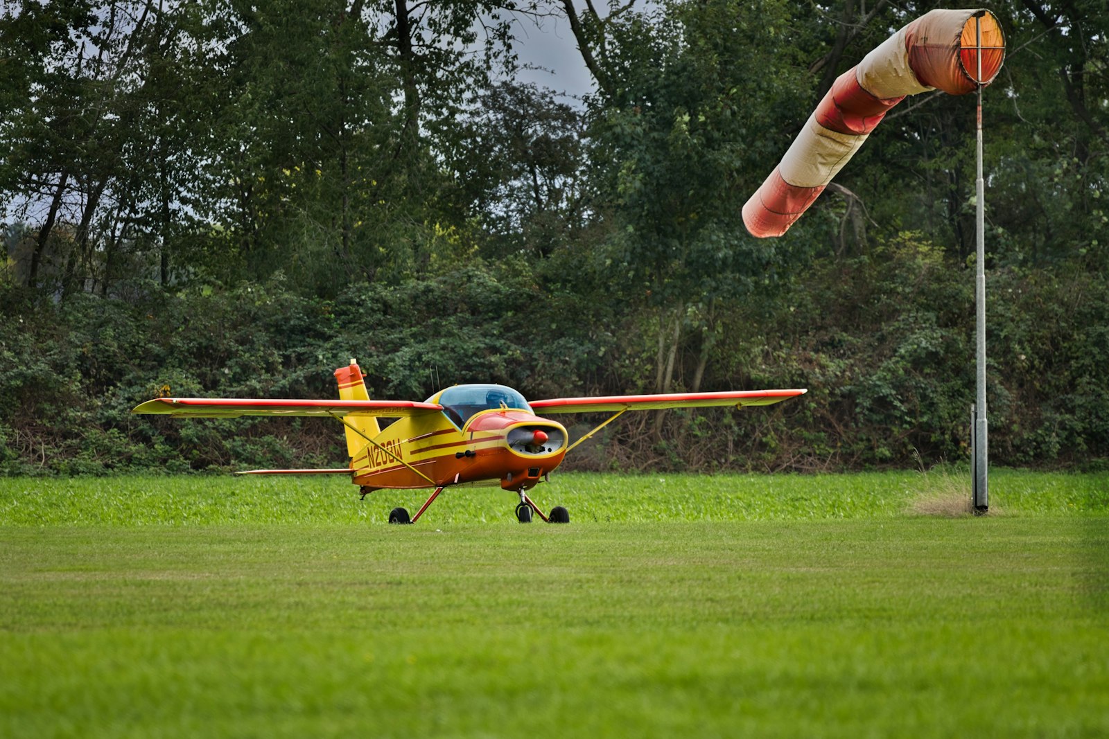 Small yellow RC airplane on grassy airfield with windsock